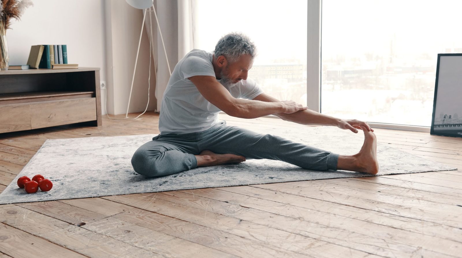 Man performing a seated forward reach as part of a flexibility and stretching routine at home